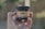 A hand with painted nails is holding a small dark jar with a beige label. The label mentions 'Full-Spectrum CBD Salve' and other details about the product. The background is blurred, suggesting an outdoor setting.