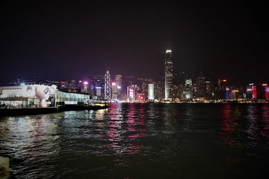 Nighttime view of Manhattan skyline with illuminated skyscrapers reflecting in the Hudson River.