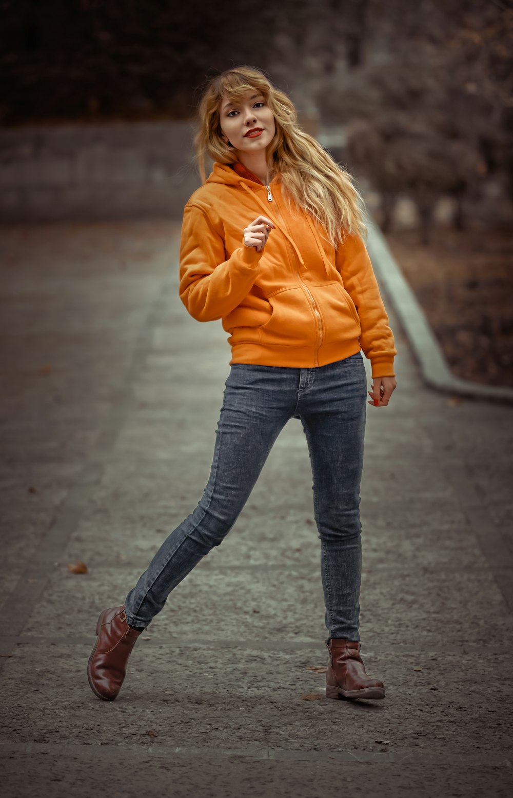 woman in orange jacket and blue jeans standing outdoors