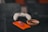 A gaming controller sits on a dark surface next to a vibrant orange smartphone and an ashtray containing a single burnt cigarette. The background is blurred, creating a cozy and relaxed atmosphere.