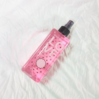 A pink spray bottle labeled with the word 'LOVE' and additional text, placed on a crumpled, white fabric surface. The bottle is transparent, allowing a glimpse of the liquid inside.
