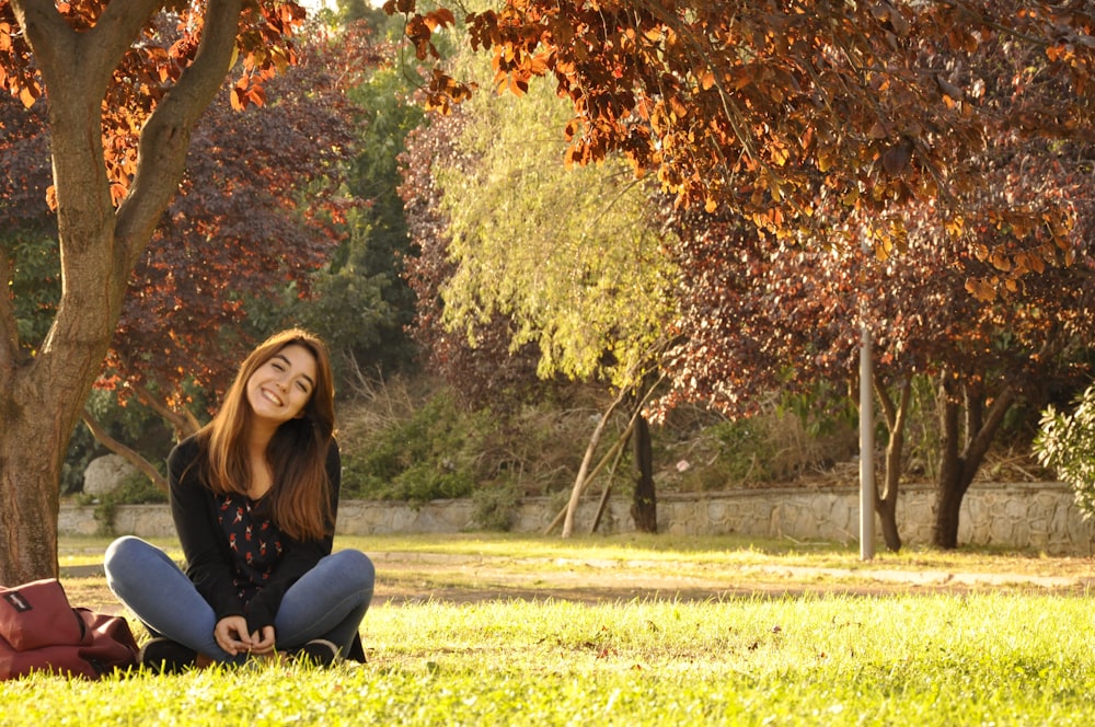shallow focus photo of woman in black long-sleeved shirt sitting on beside tree