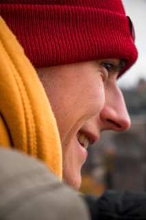 Close-up of a vibrant red wool beret worn by a smiling person outdoors on a crisp day.