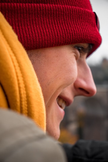 Close-up of a vibrant red wool beret worn by a smiling person outdoors on a crisp day.