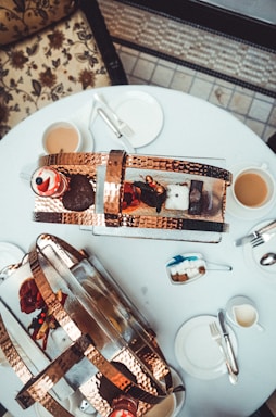 A cozy table set with an assortment of tea snacks including scones, sandwiches, and cookies alongside a steaming teapot.