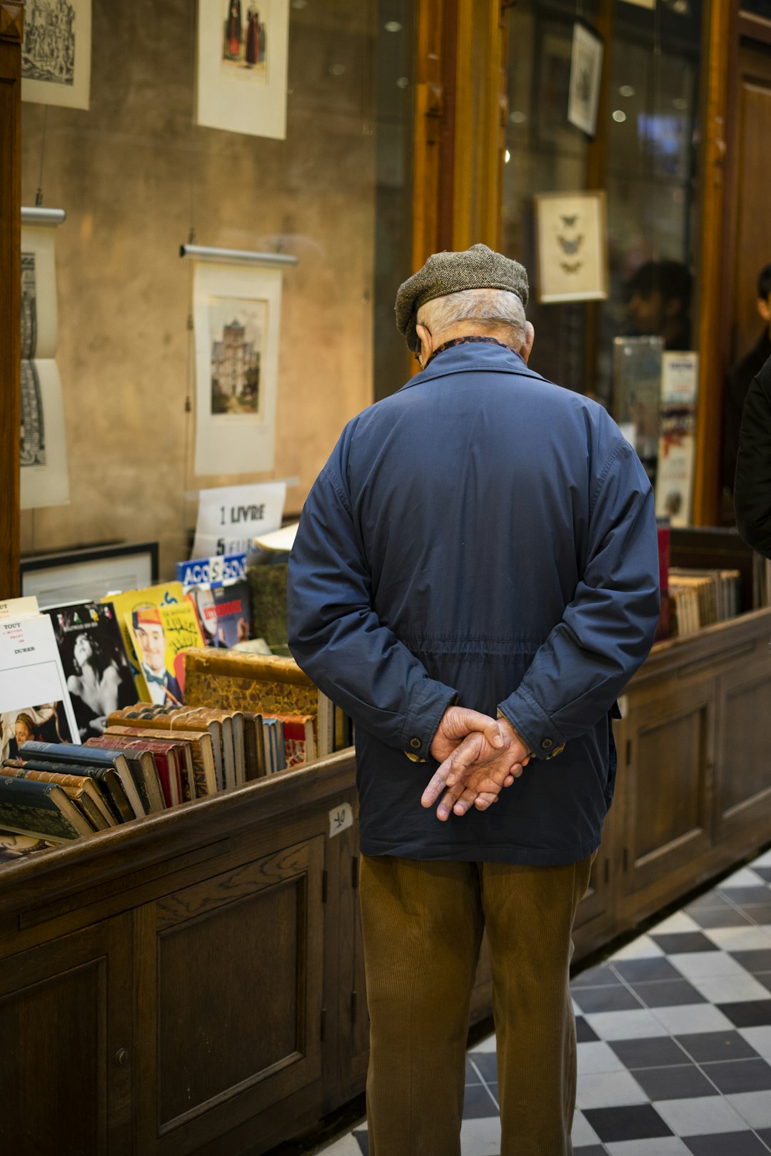 man wearing blue jacket standing near bookshelf