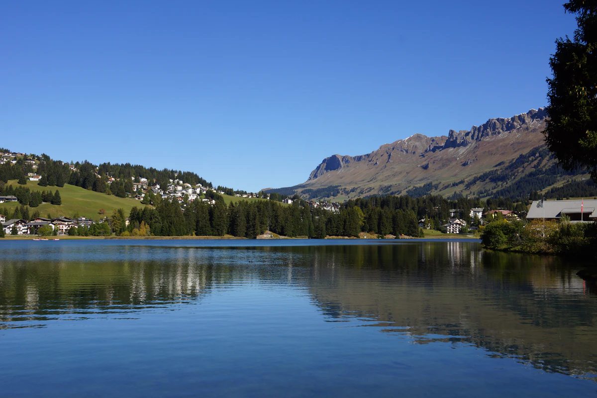 The Heidsee at Lenzerheide in autumn, with houses on the far shore and a rocky ridge behind