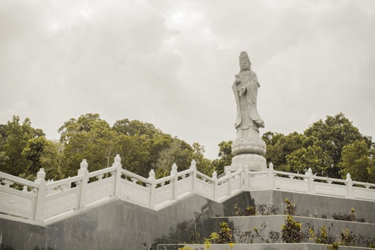 Buddha standing surrounded with green trees under gray sky in Belitung Indonesia