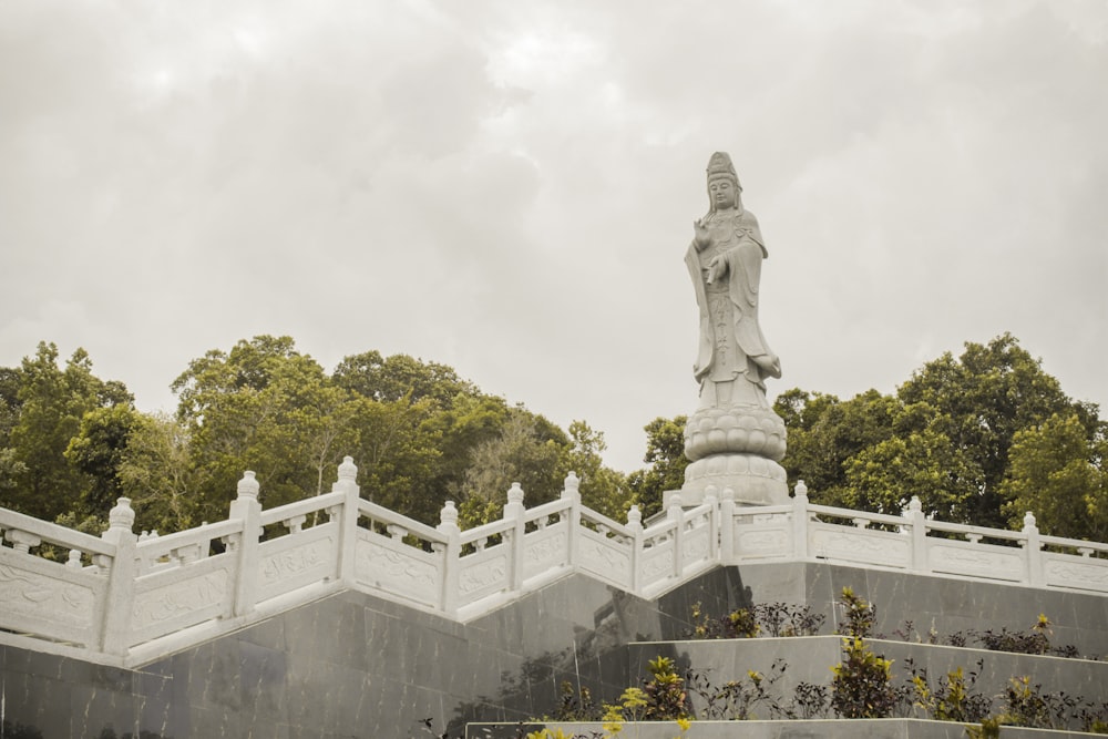 Buddha standing surrounded with green trees under gray sky