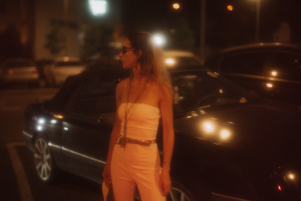 woman wearing white tube standing near black vehicle during night time