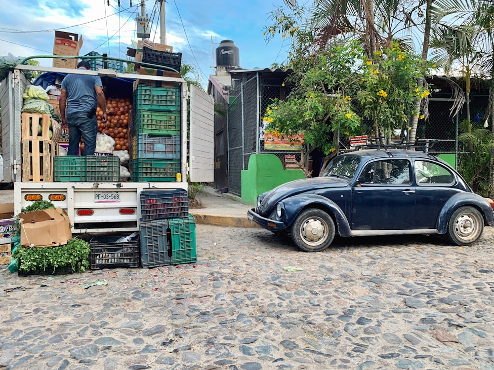 blue Volkswagen coupe parking near road and man standing in front of truck under blue and white sky