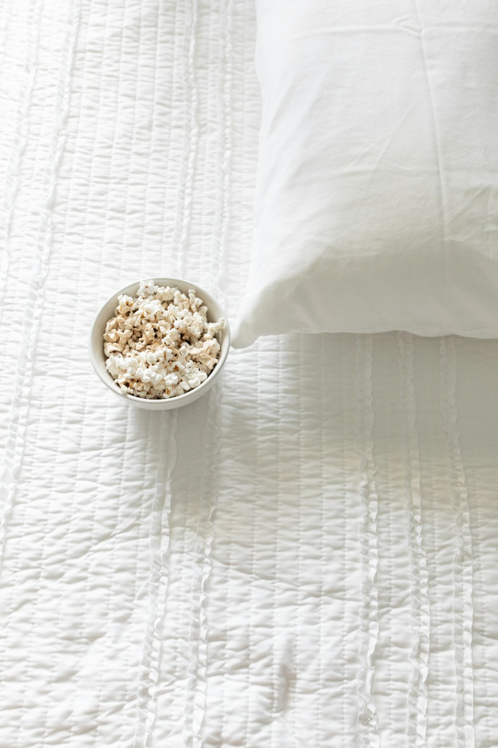 popcorn in round white bowl on bed