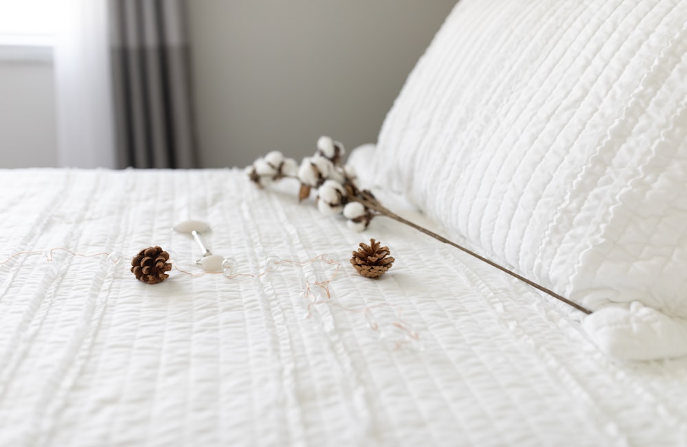 two brown pinecones near white cotton on bed