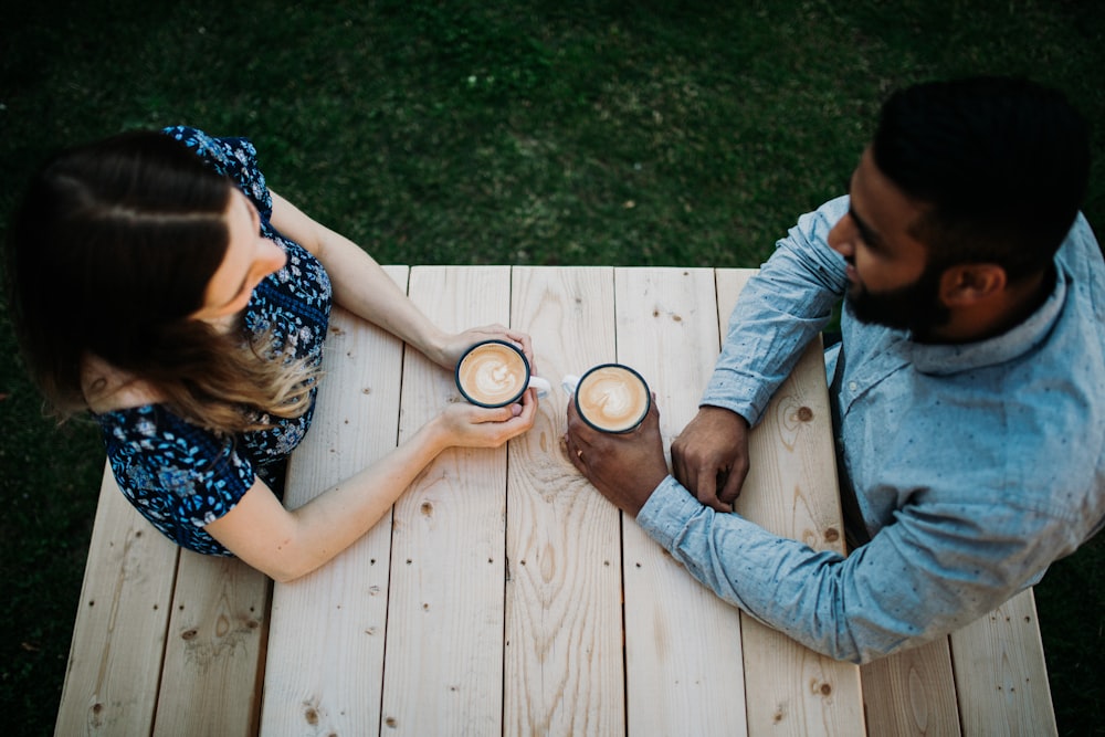 man and woman sitting at table while holding mugs