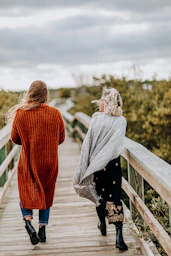 two women walking on brown wooden bridge during daytime