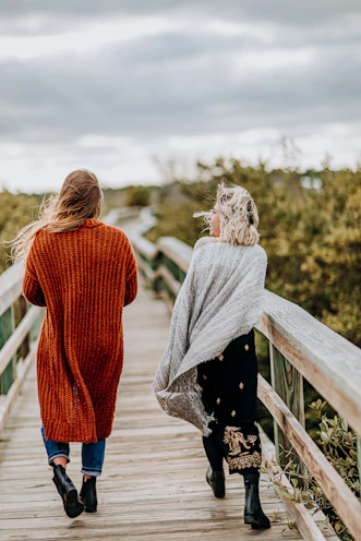 two women walking on brown wooden bridge during daytime