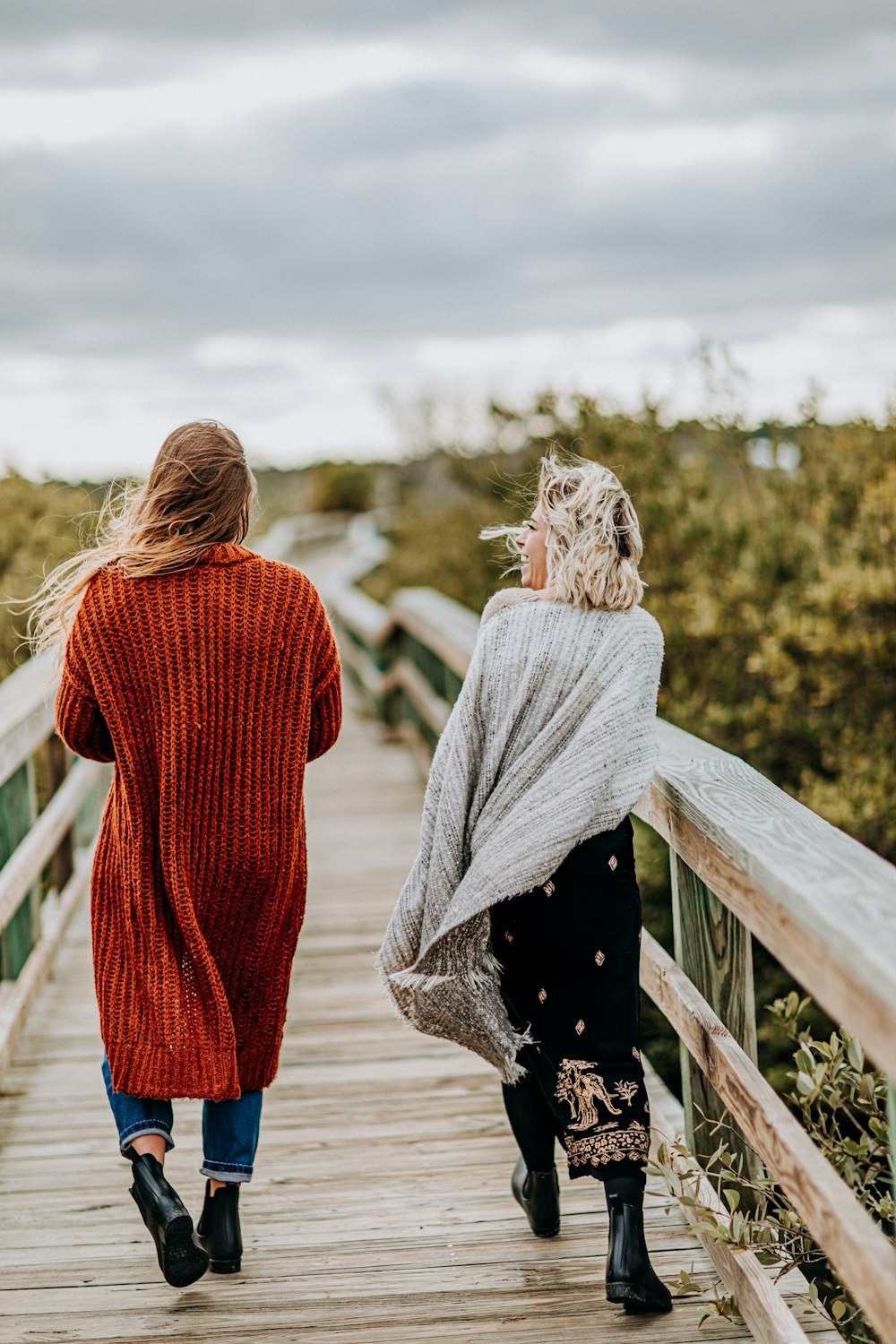 two women walking on brown wooden bridge during daytime