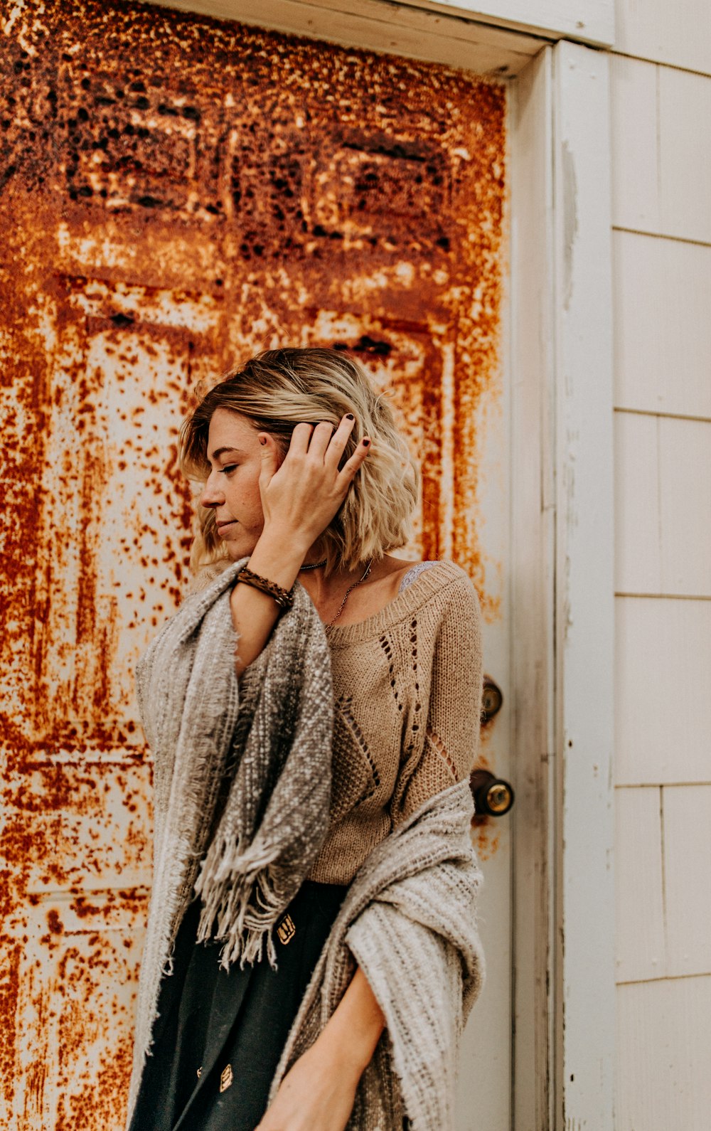 woman wearing brown sweater while standing and fixing her hair