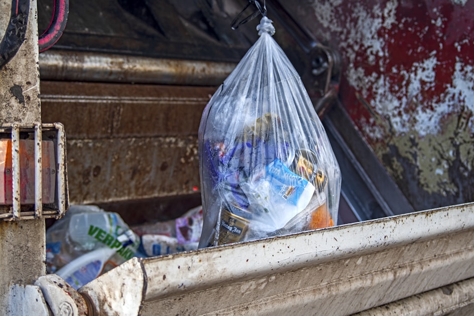 Rear-loading garbage truck on a residential street in morning light showing waste management equipment