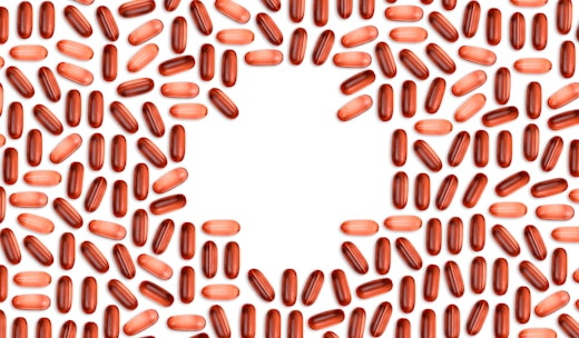 Numerous red and pink capsules are arranged in a pattern that forms the shape of a heart in the center of the image with a white background.