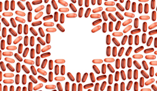 Numerous red and pink capsules are arranged in a pattern that forms the shape of a heart in the center of the image with a white background.