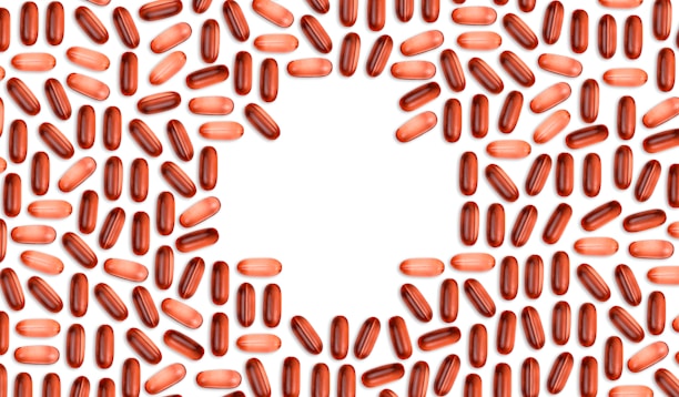 Numerous red and pink capsules are arranged in a pattern that forms the shape of a heart in the center of the image with a white background.