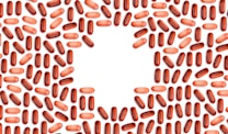 Numerous red and pink capsules are arranged in a pattern that forms the shape of a heart in the center of the image with a white background.