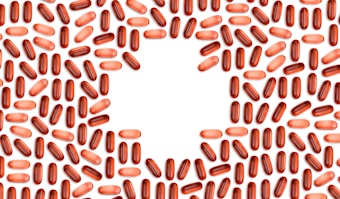 Numerous red and pink capsules are arranged in a pattern that forms the shape of a heart in the center of the image with a white background.