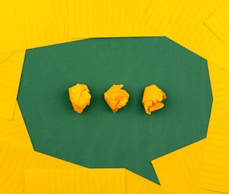 three crumpled yellow papers on green surface surrounded by yellow lined papers