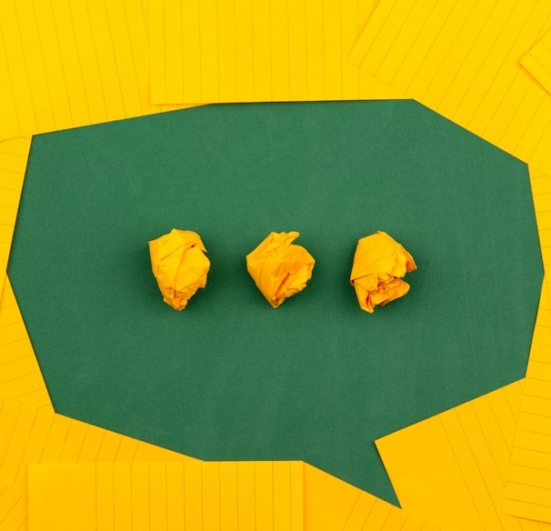 three crumpled yellow papers on green surface surrounded by yellow lined papers