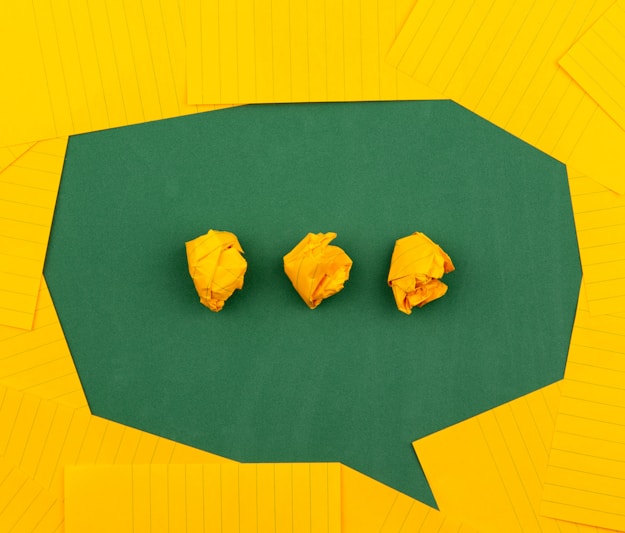 three crumpled yellow papers on green surface surrounded by yellow lined papers