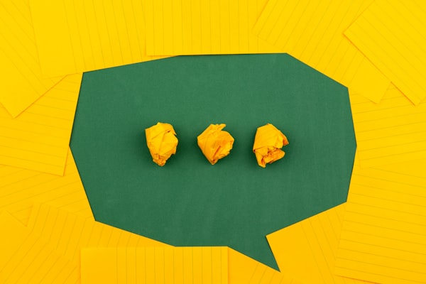 a "chat" icon made from yellow lined paper surrounding a green space with three balled up pieces of yellow paper