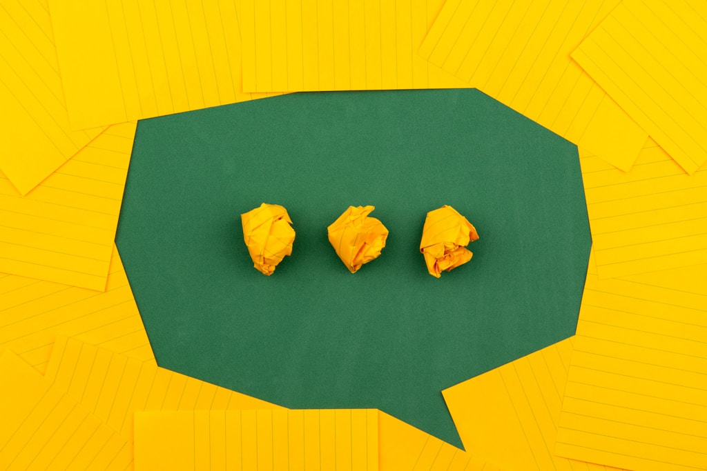 Performance review comments: three crumpled yellow papers on green surface surrounded by yellow lined papers