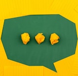 three crumpled yellow papers on green surface surrounded by yellow lined papers