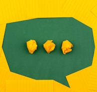 three crumpled yellow papers on green surface surrounded by yellow lined papers