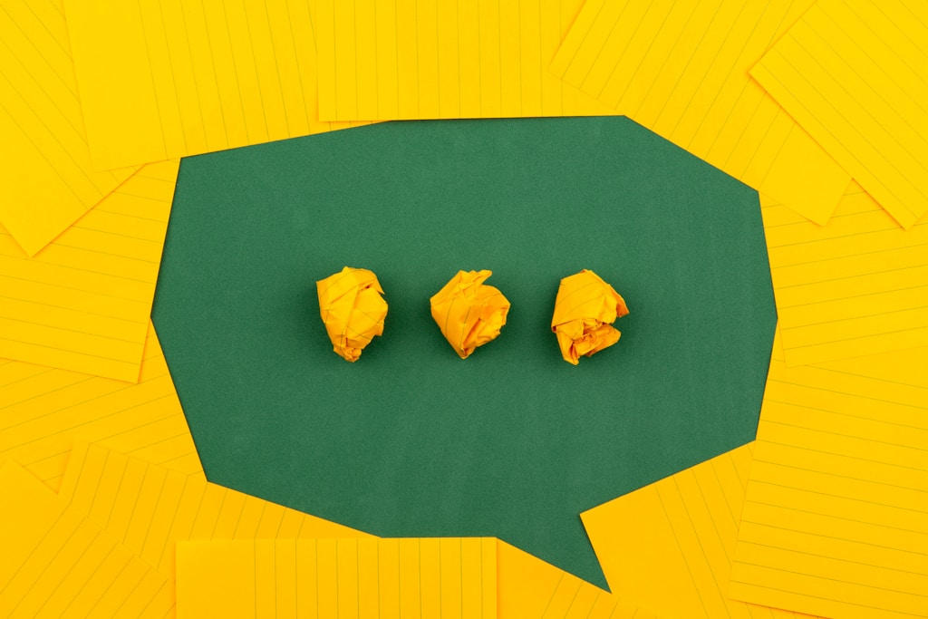 Performance review comments: three crumpled yellow papers on green surface surrounded by yellow lined papers