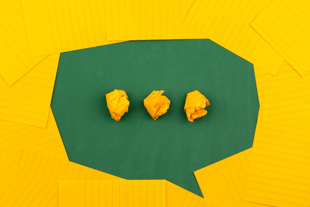 three crumpled yellow papers on green surface surrounded by yellow lined papers