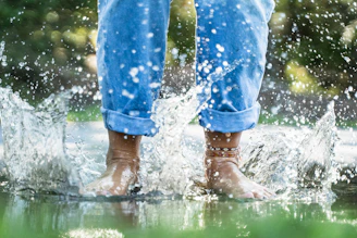 person in blue jeans splashing water through feet
