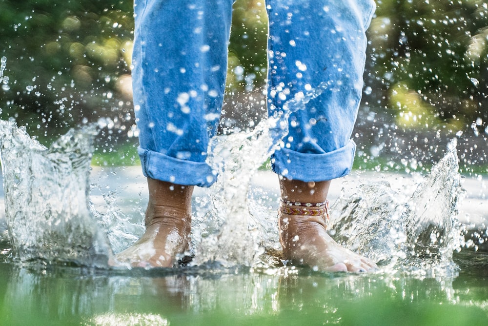 person in blue jeans splashing water through feet