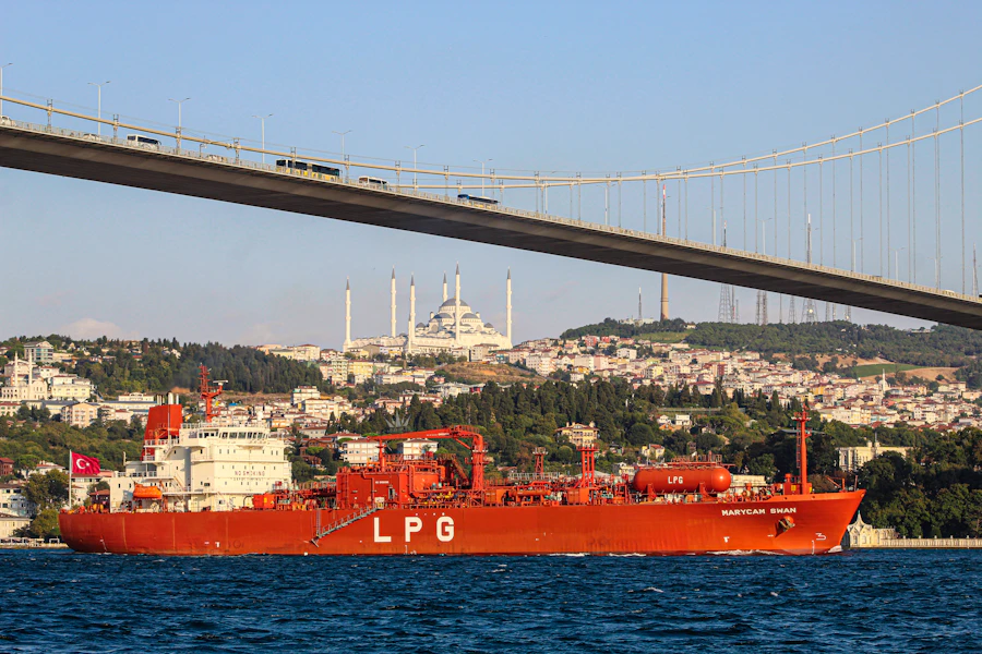 Red LPG tanker vessel passing beneath a bridge, available for charter