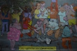 A colorful mural depicts a crowd of animated characters engaged in a mix of emotions. Some individuals appear to be in a celebratory mood, while others are bent over a skeleton on the ground in a more somber or introspective manner. The scene is filled with diverse characters exhibiting a range of expressions and actions.