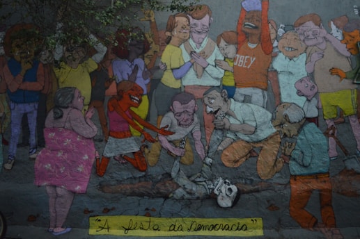 A colorful mural depicts a crowd of animated characters engaged in a mix of emotions. Some individuals appear to be in a celebratory mood, while others are bent over a skeleton on the ground in a more somber or introspective manner. The scene is filled with diverse characters exhibiting a range of expressions and actions.