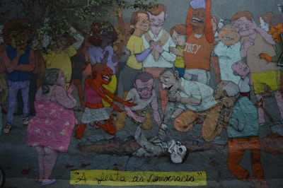 A colorful mural depicts a crowd of animated characters engaged in a mix of emotions. Some individuals appear to be in a celebratory mood, while others are bent over a skeleton on the ground in a more somber or introspective manner. The scene is filled with diverse characters exhibiting a range of expressions and actions.
