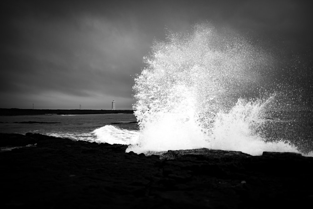 grayscale photo of splashing water n boulder