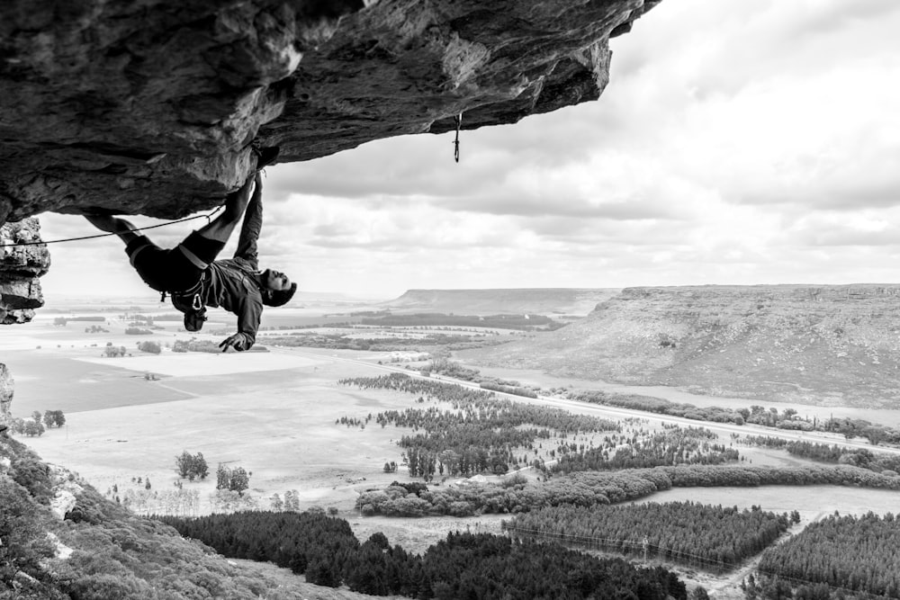 grayscale photo of man rock climbing