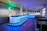 A modern, retro-style diner with a neon-lit bar and chrome stools, featuring a checkerboard floor pattern. The interior includes sleek black booths and a welcoming atmosphere accentuated by soft blue lighting. A sign on the wall reads 'Circuit Mallorca' alongside vintage decor elements.