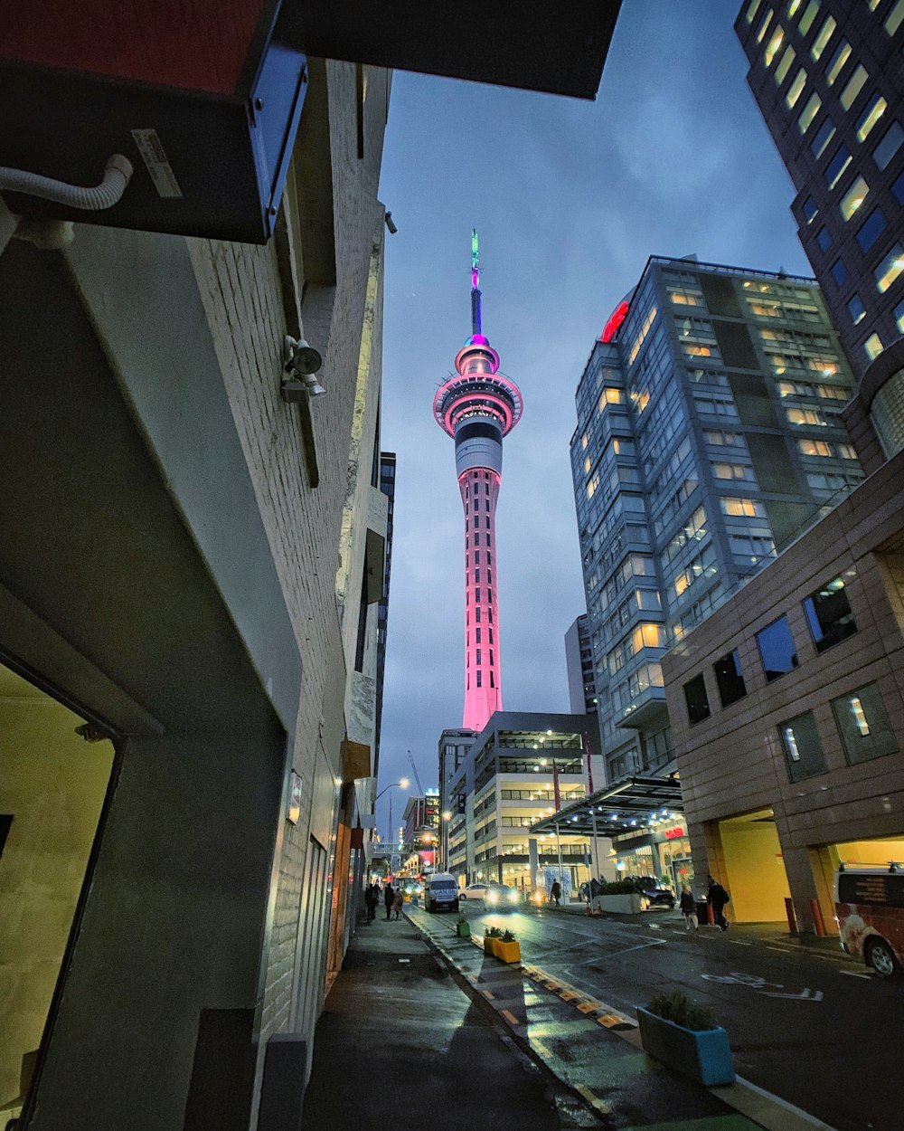 people walking on pathway near buildings and different vehicles on road during night time