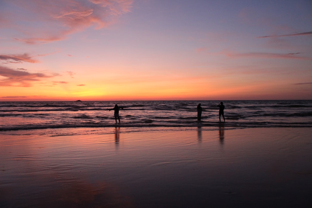 three people on seashore during golden hour