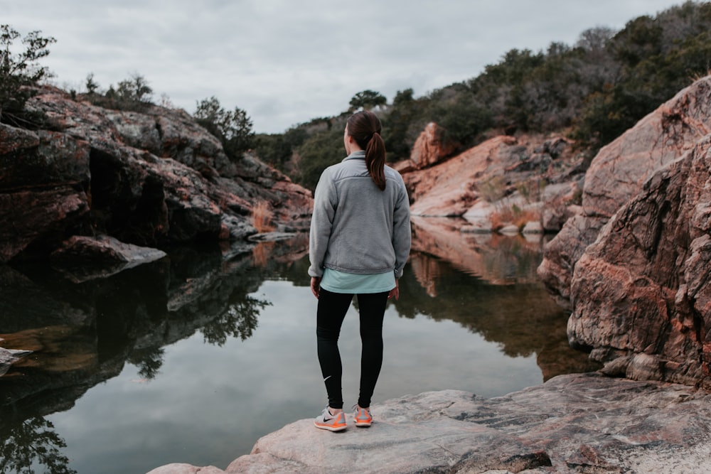 woman standing on rock beside body of water during daytime