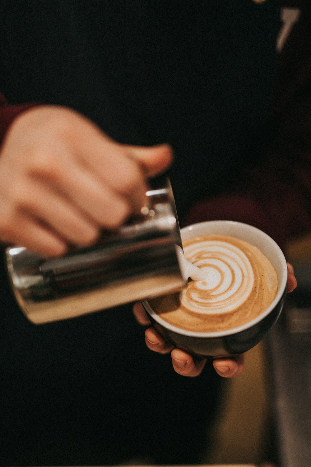 person pouring latte in mug